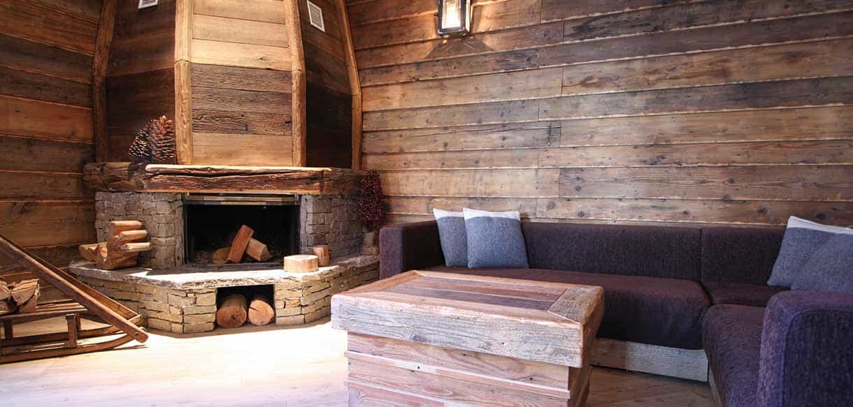 Wohnraum mit Natursteinkamin, Holzwänden und Sofa in einem Appartement der Ferienwohnanlage Pragelato
