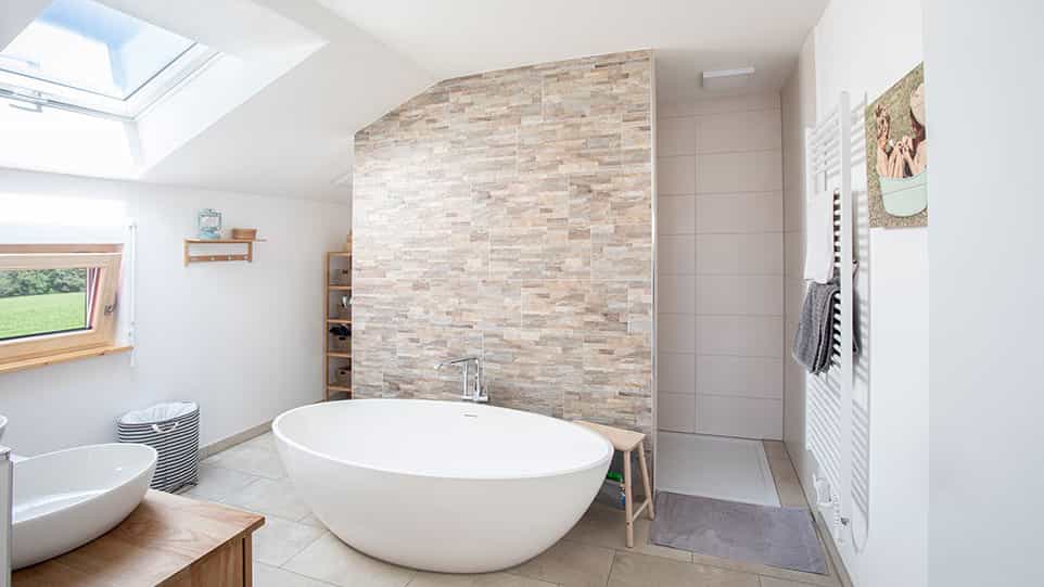 Bad mit freistehender Wanne, Natursteinwand und Dachfenster im Haas Fertighaus der Familie Kroiß