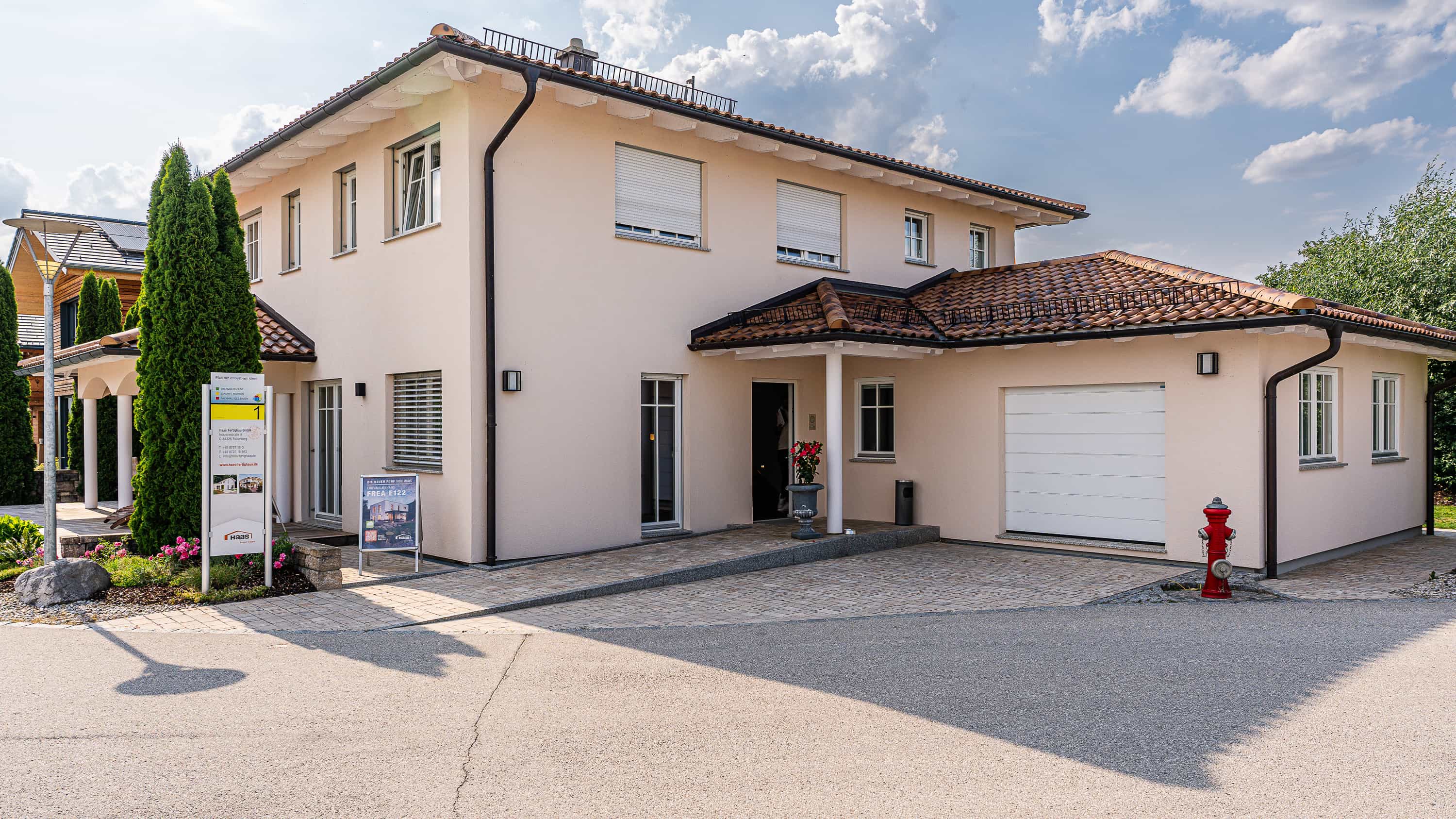 Eingangsseite des Musterhauses Haas MH Poing 187 mit Terrakottadach, Garage und Infotafel