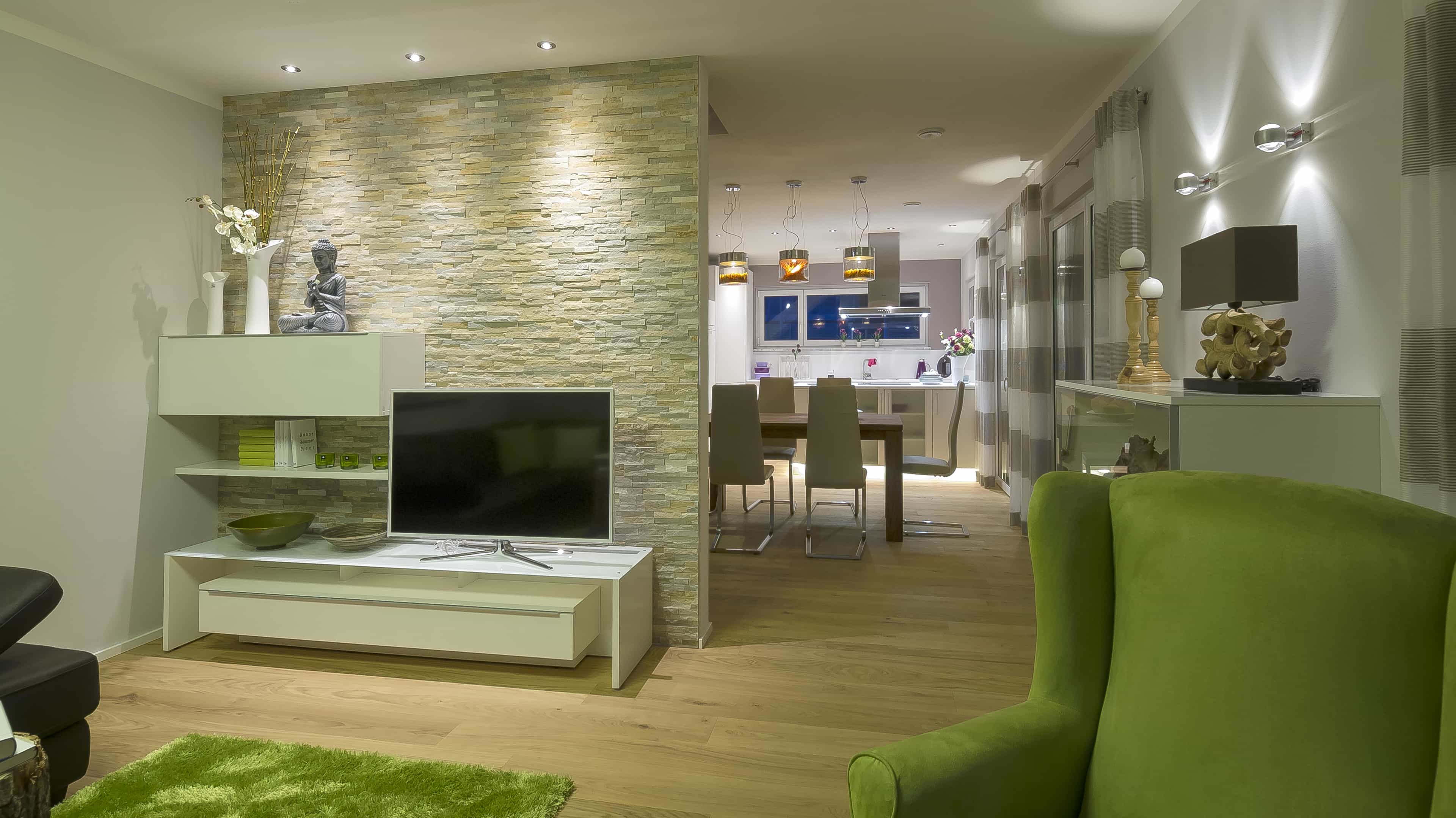 Wohnbereich mit Natursteinwand, TV-Lowboard und Blick zum Essplatz im Musterhaus Haas MH Mannheim J 159