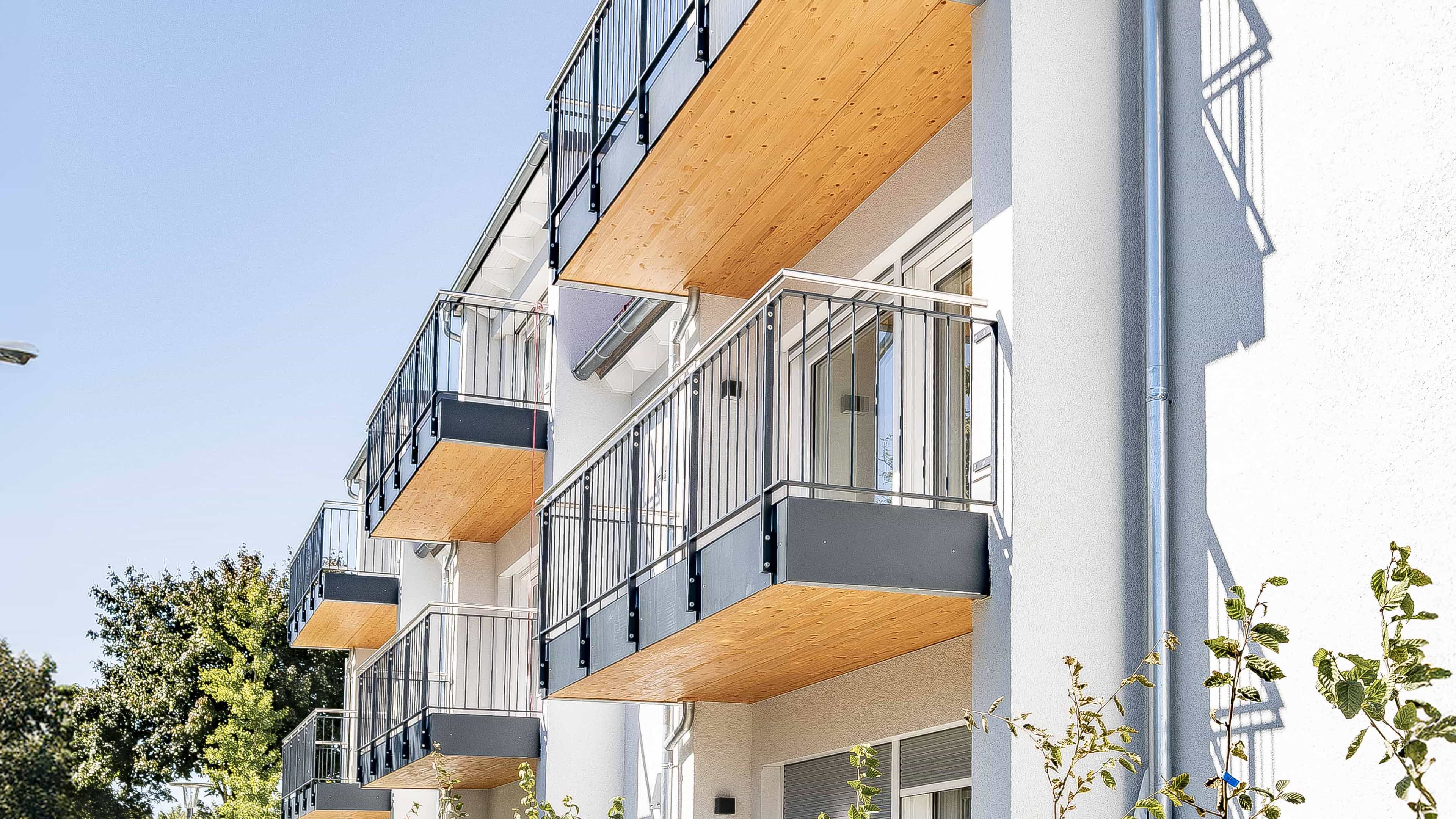 Balkone mit Holzuntersicht und Metallgeländer an der weißen Fassade der Wohnanlage in Eching