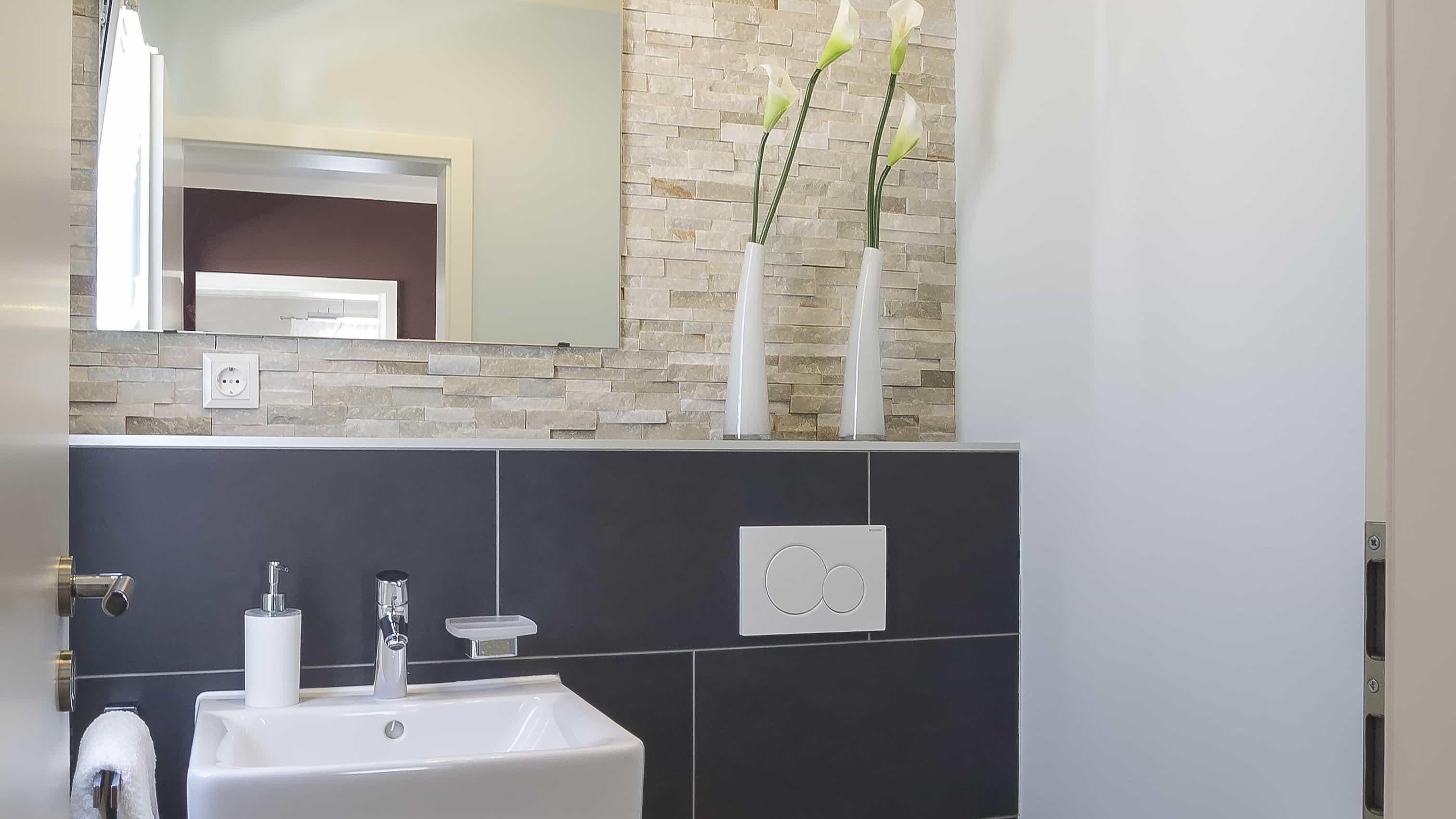 Gäste-WC mit Waschbecken, Natursteinwand und dunklen Fliesen im Musterhaus Haas MH Mannheim J 159