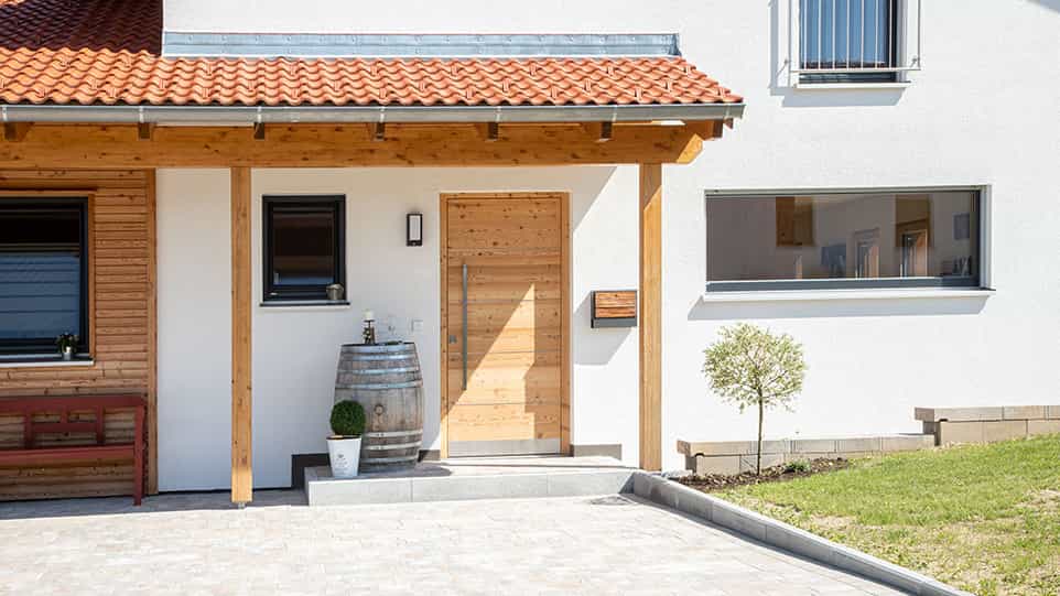 Hauseingang mit Holzvordach, Holztür und Holzfass am Fertighaus der Familie Kroiß