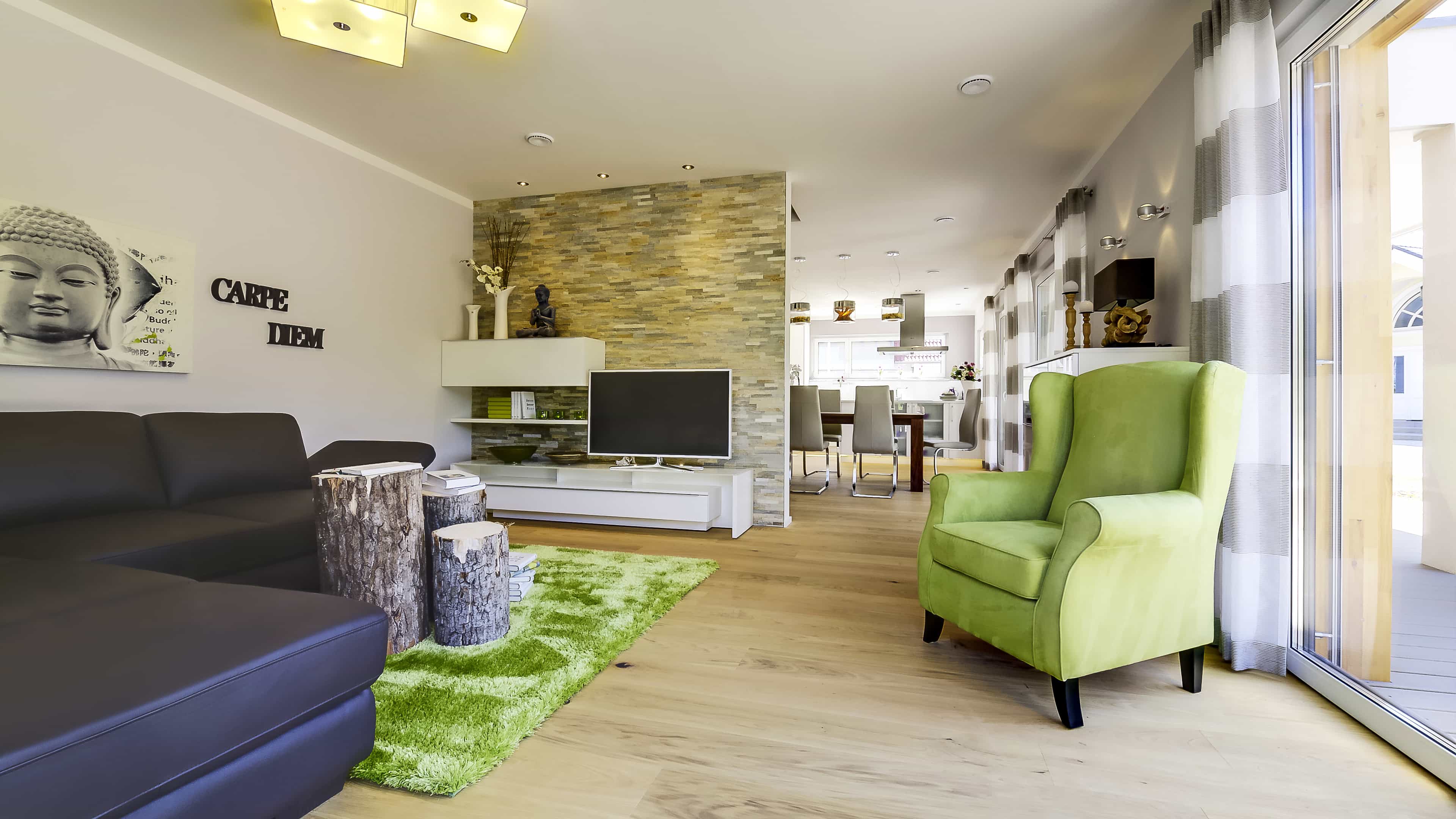 Wohn-Essbereich mit dunklem Sofa, grünem Ohrensessel und Esstisch im Musterhaus Haas MH Mannheim J 159
