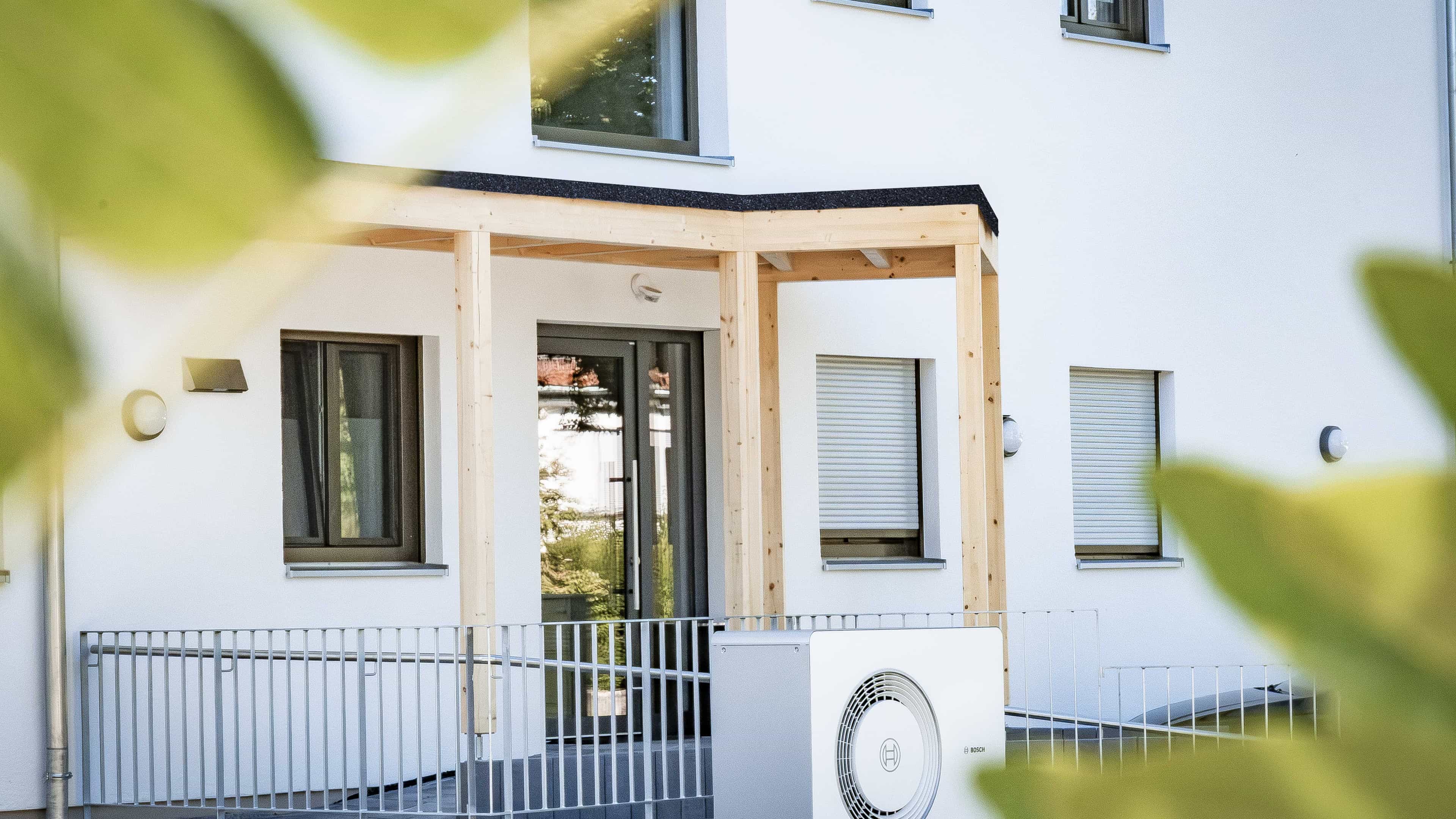Weißer Hauseingang mit Holzvordach und Wärmepumpen-Außengerät an der Wohnanlage in Eichendorf von Haas Wohnbau