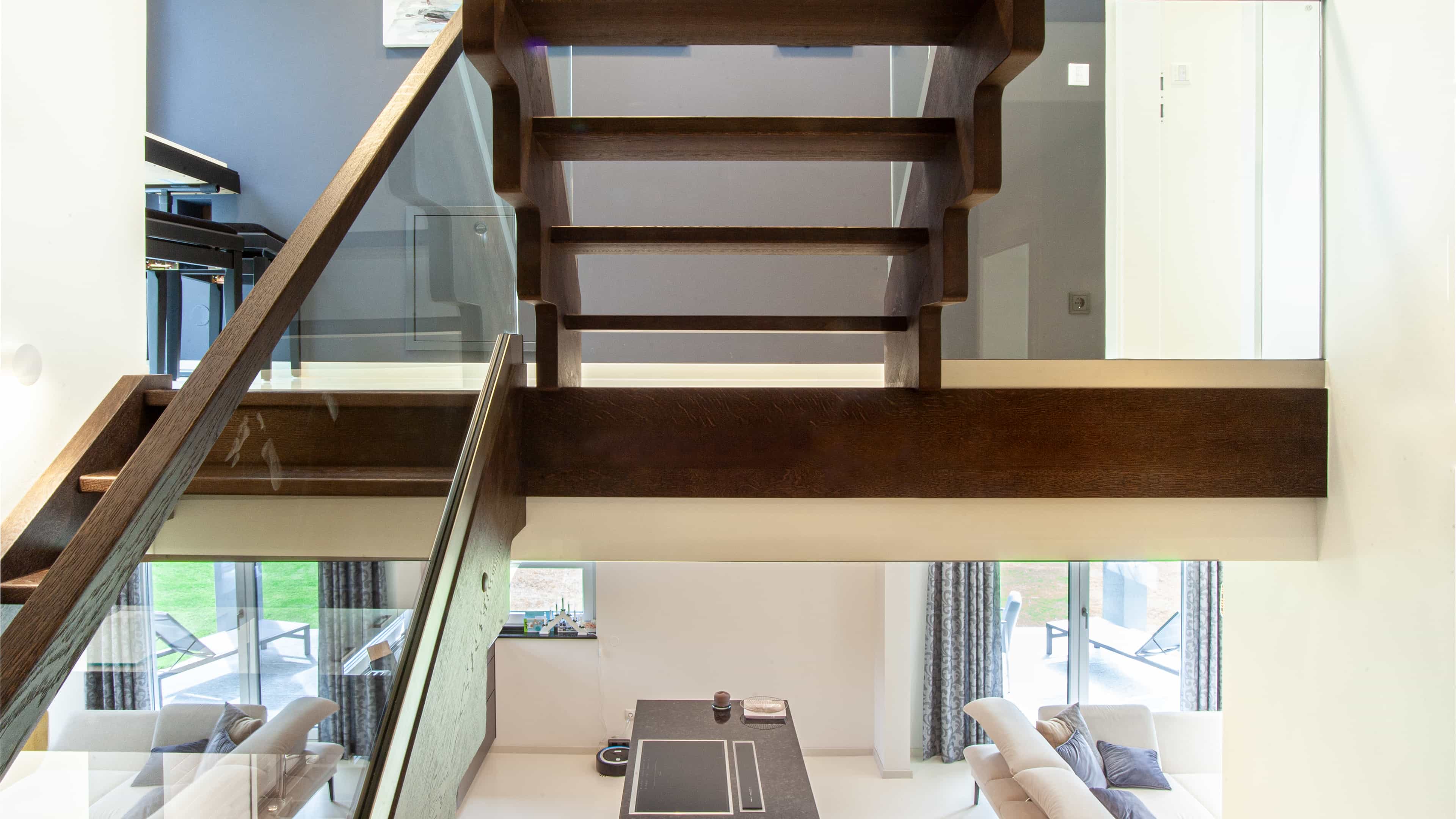 Dunkle Holztreppe mit Glasgeländer und Blick hinunter in den Wohnraum des modernen Haas Ferienhauses