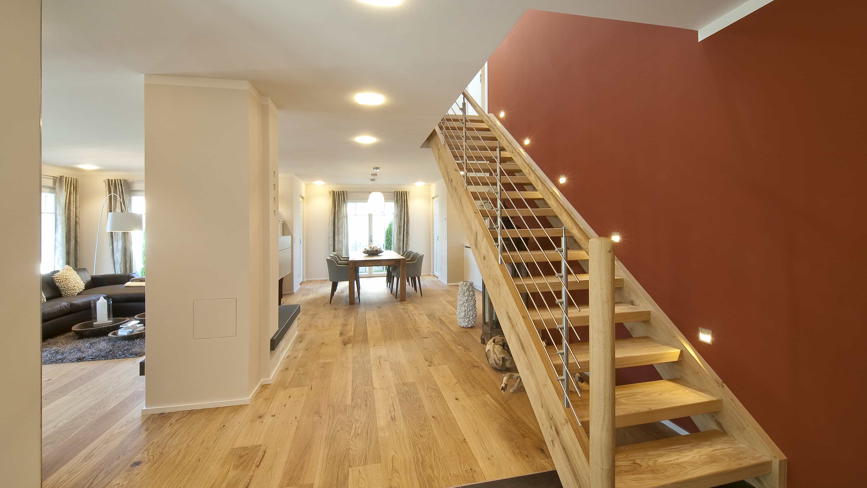 Offene Holztreppe vor roter Wand mit Blick in den Wohnbereich im Musterhaus Haas MH Poing 187
