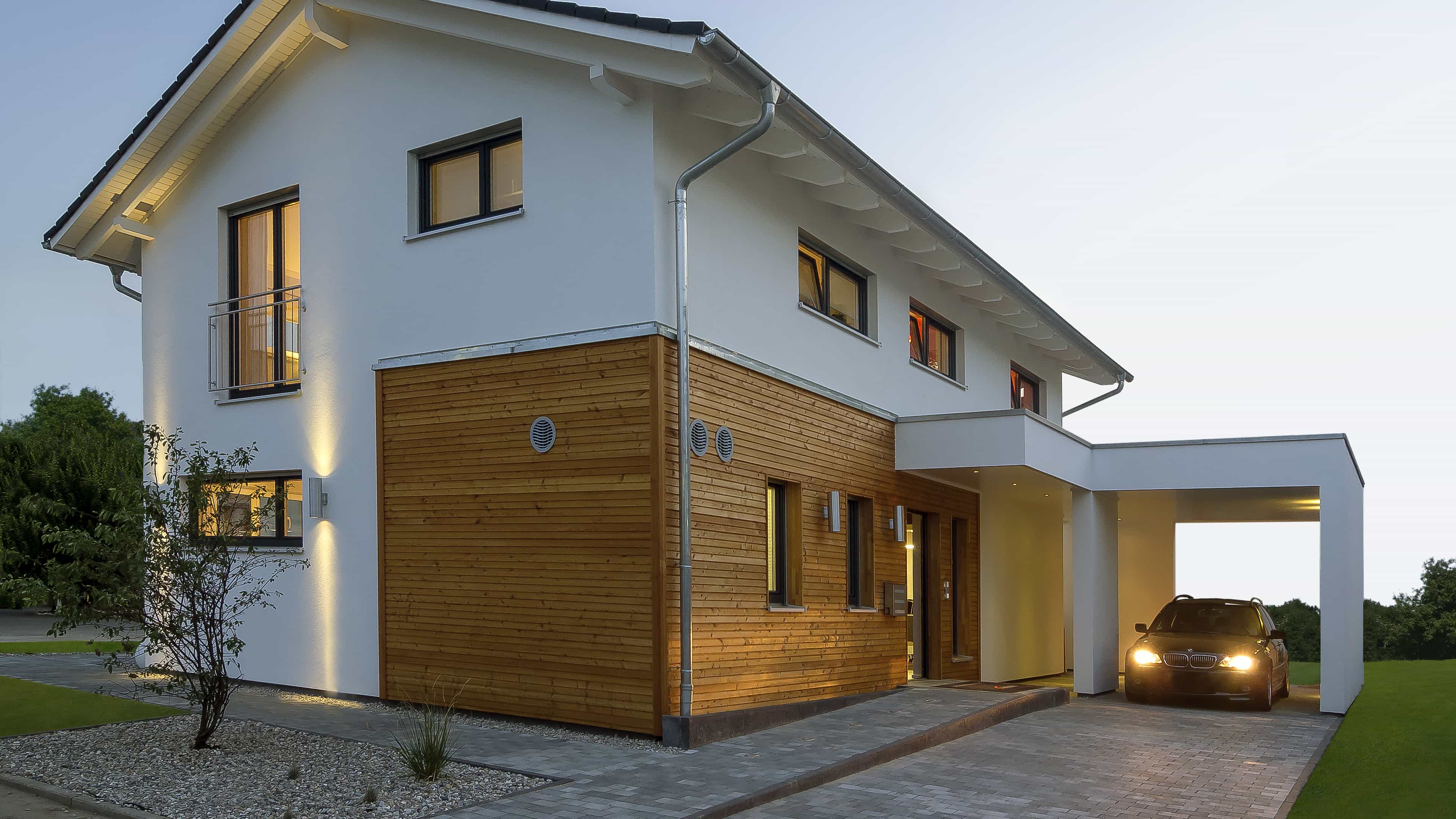 Musterhaus Haas MH Mannheim J 159 mit beleuchteten Fenstern und Carport am Abend