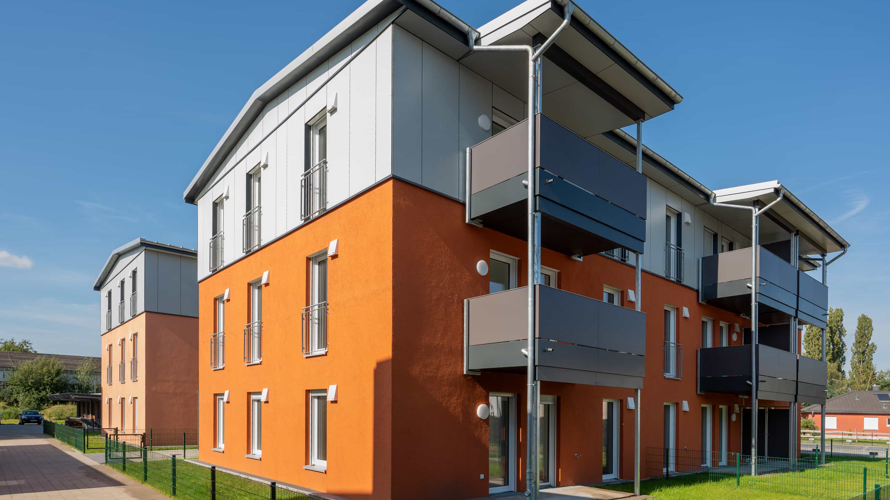 Mehrfamilienhaus mit orangefarbener Fassade und Balkonen im Wohnquartier Zum Glück Bötzow von Haas