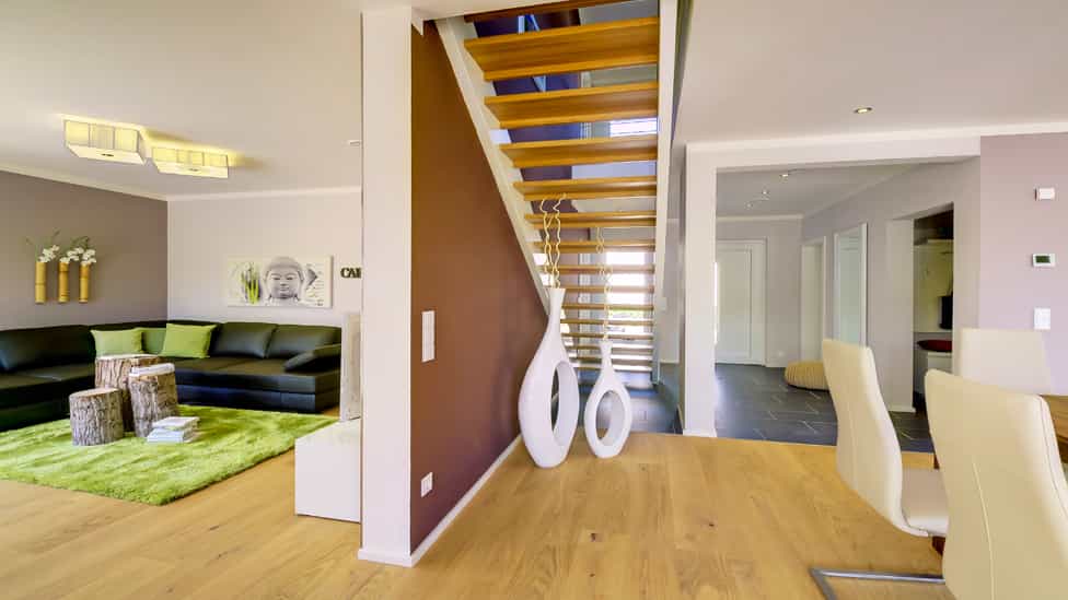 Wohnbereich mit offener Holztreppe, Sofa und grünem Teppich im Musterhaus Haas MH Mannheim J 159