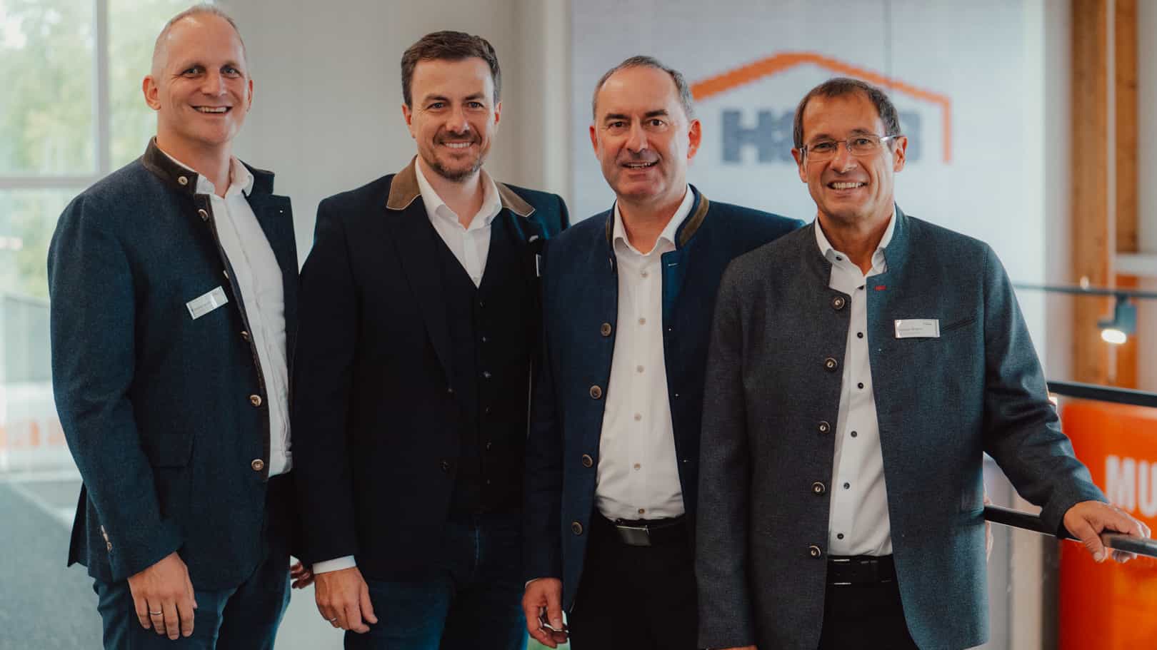 Vier Männer in Anzügen beim Gruppenfoto vor dem Haas Logo, Startschuss der Initiative Holz Rettet Klima