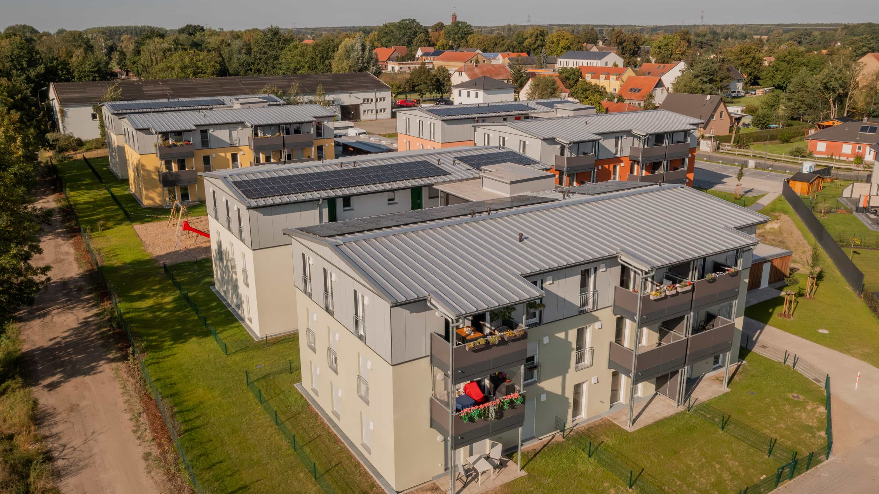 Luftaufnahme der sechs Mehrfamilienhäuser mit Flachdächern im Wohnquartier Zum Glück Bötzow