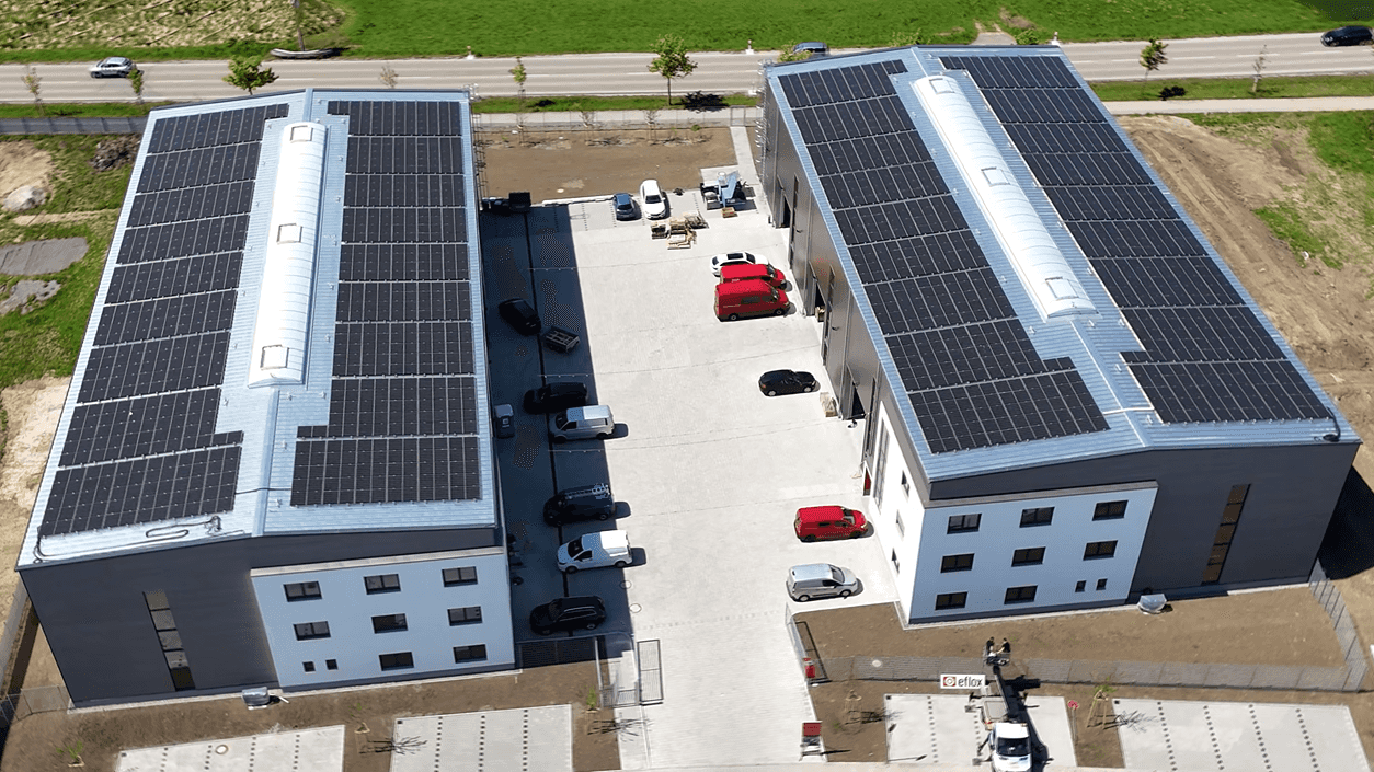 Luftaufnahme der zwei gespiegelten Lagerhallen mit Büro und Photovoltaikdächern für Dr. Joachim G. Wünning