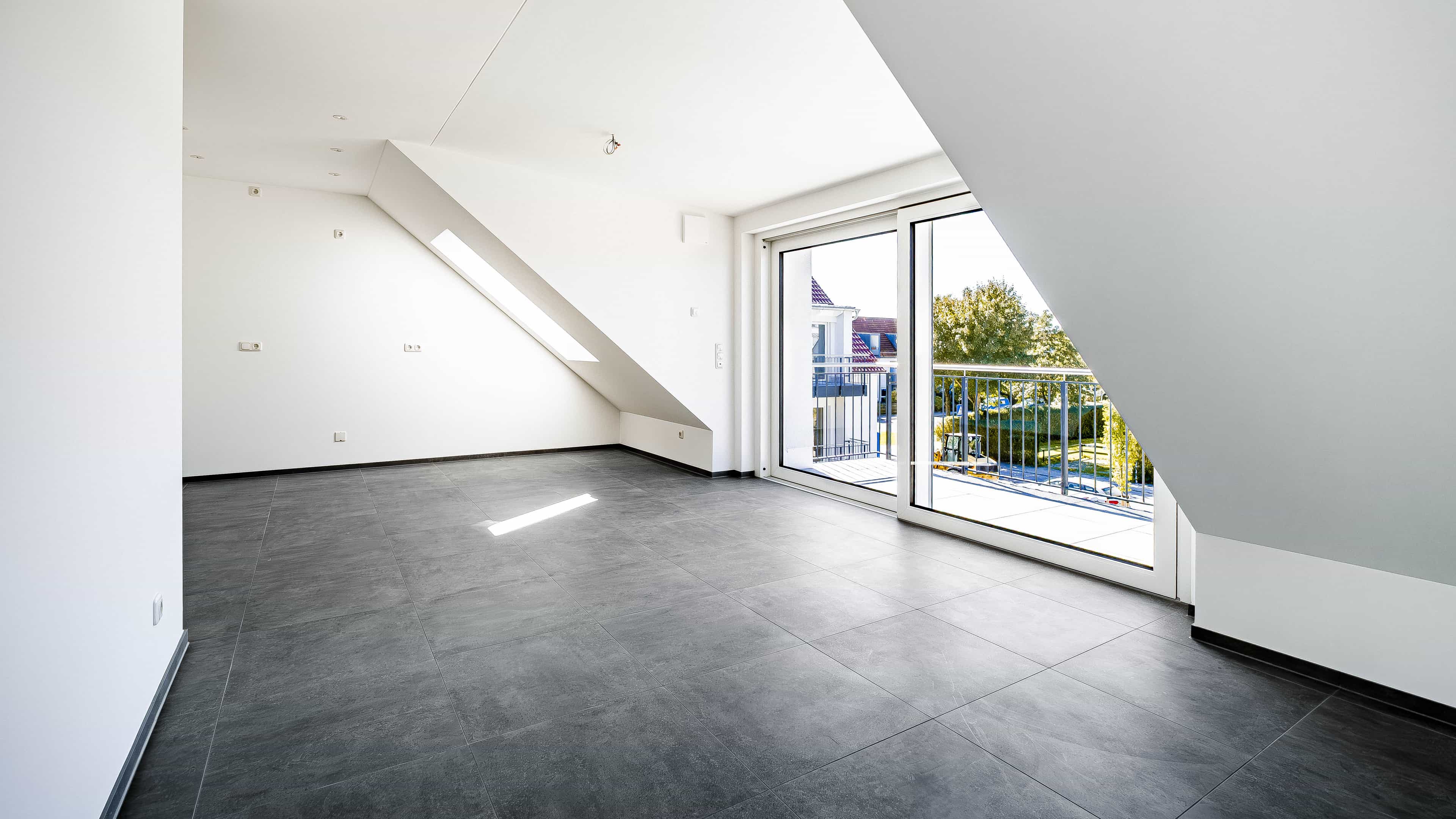 Leere Dachgeschosswohnung mit Dachschräge, dunklen Fliesen und Balkontür in der Wohnanlage Eching