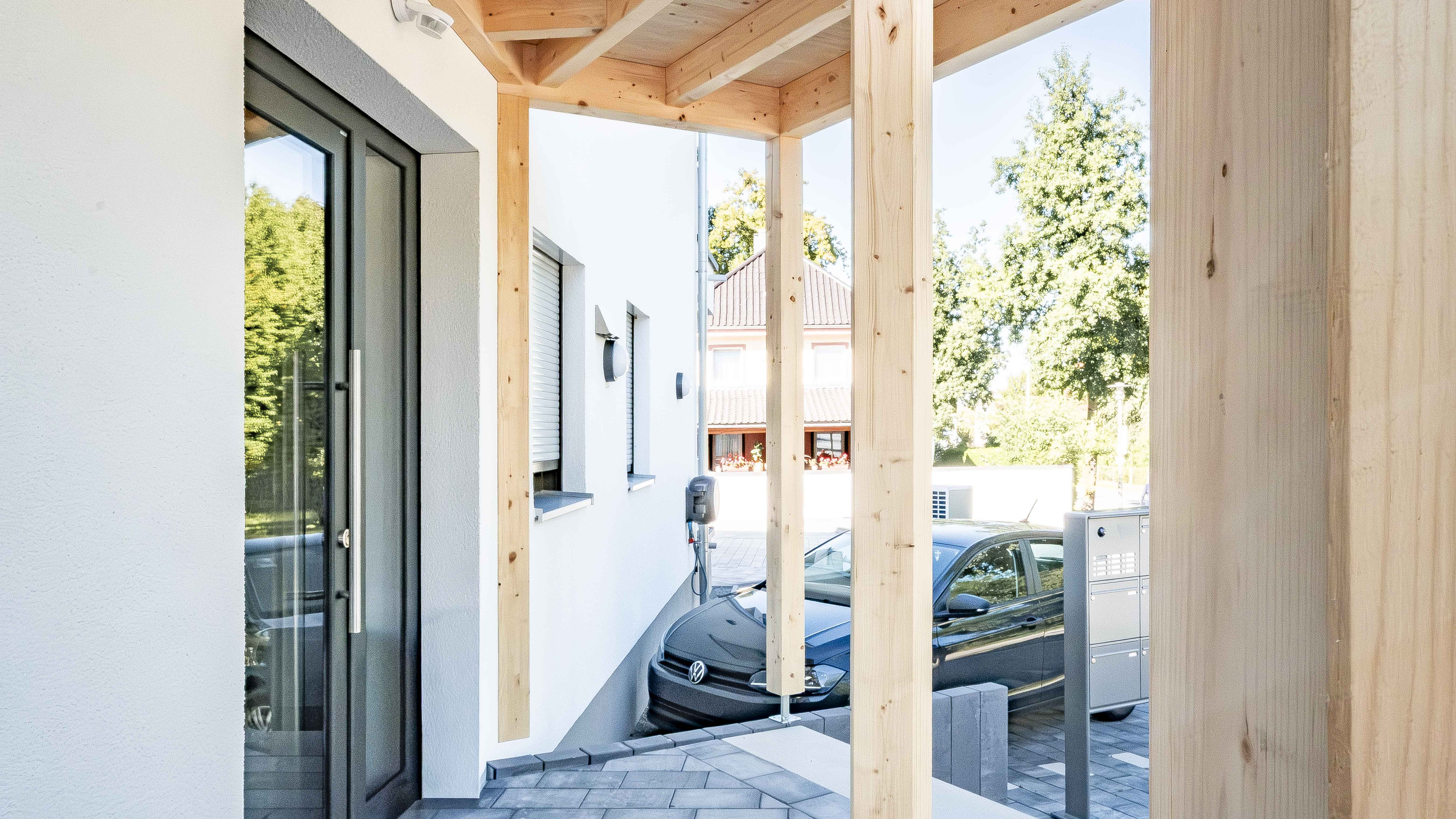 Eingangsbereich mit Holzstützen und Glastür an der Wohnanlage in Eichendorf von Haas Wohnbau