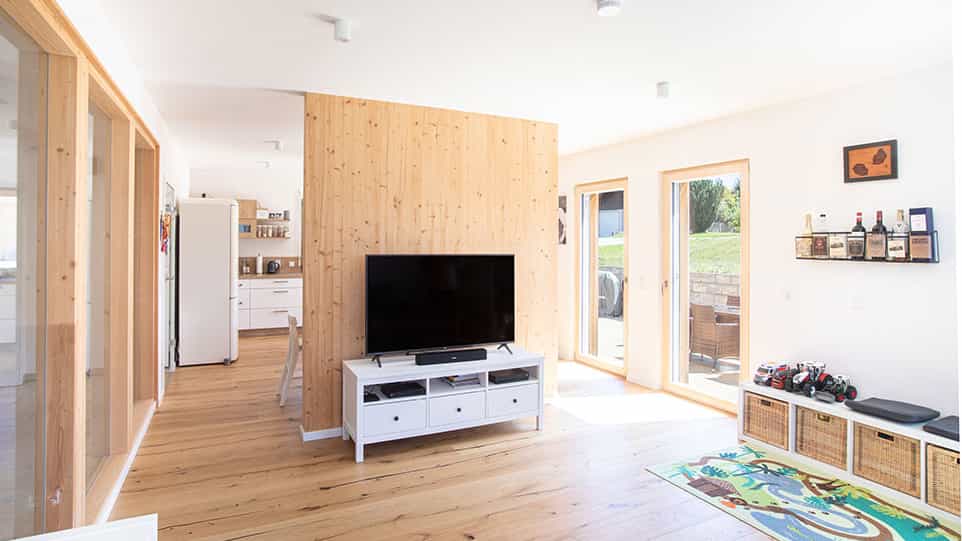 Offener Wohnbereich mit Holzwand, Fernseher und Küchenblick im Haus der Familie Kroiß