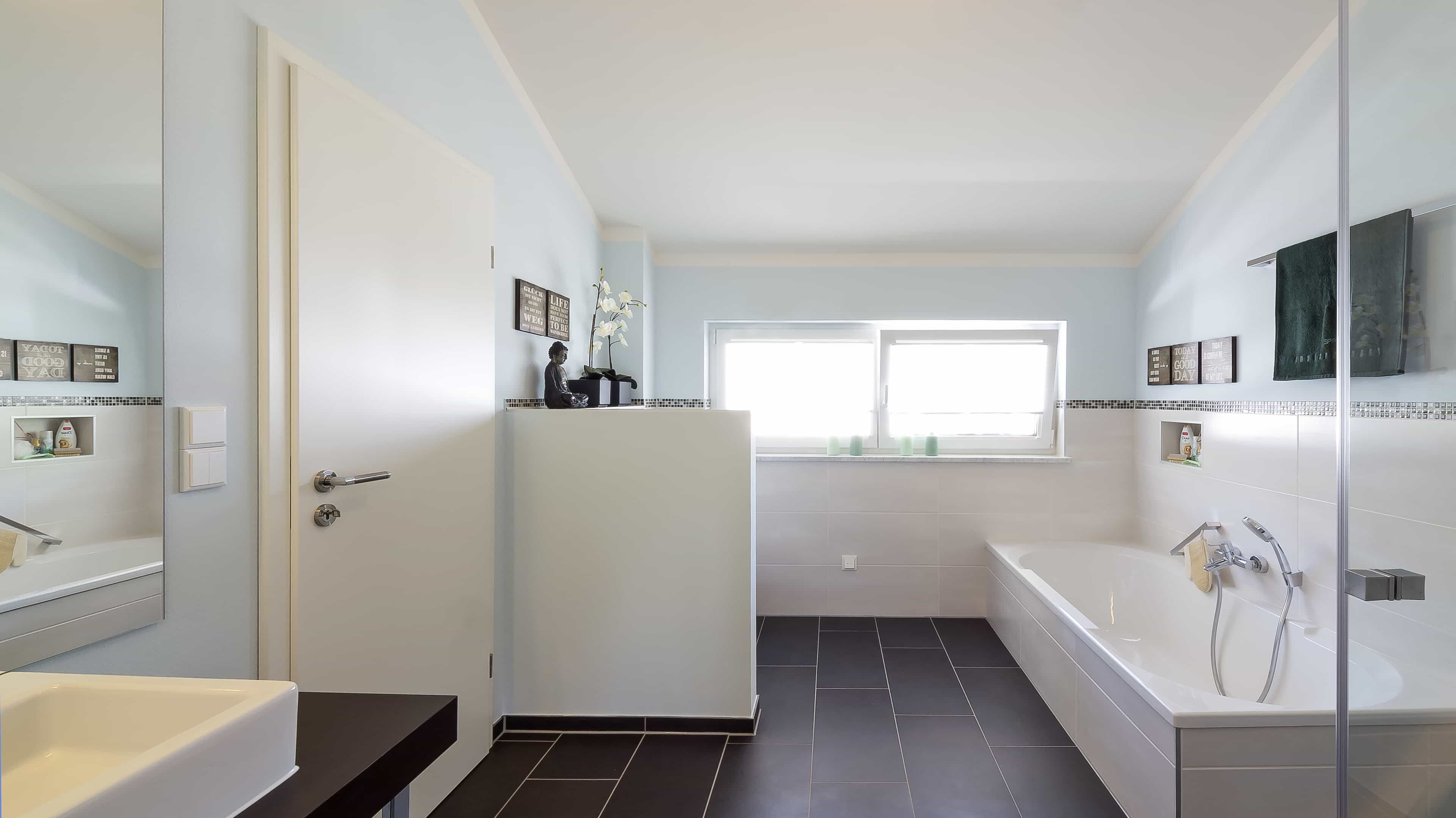 Badezimmer mit Badewanne, Fenster und dunklen Fliesen im Musterhaus Haas MH Mannheim J 159