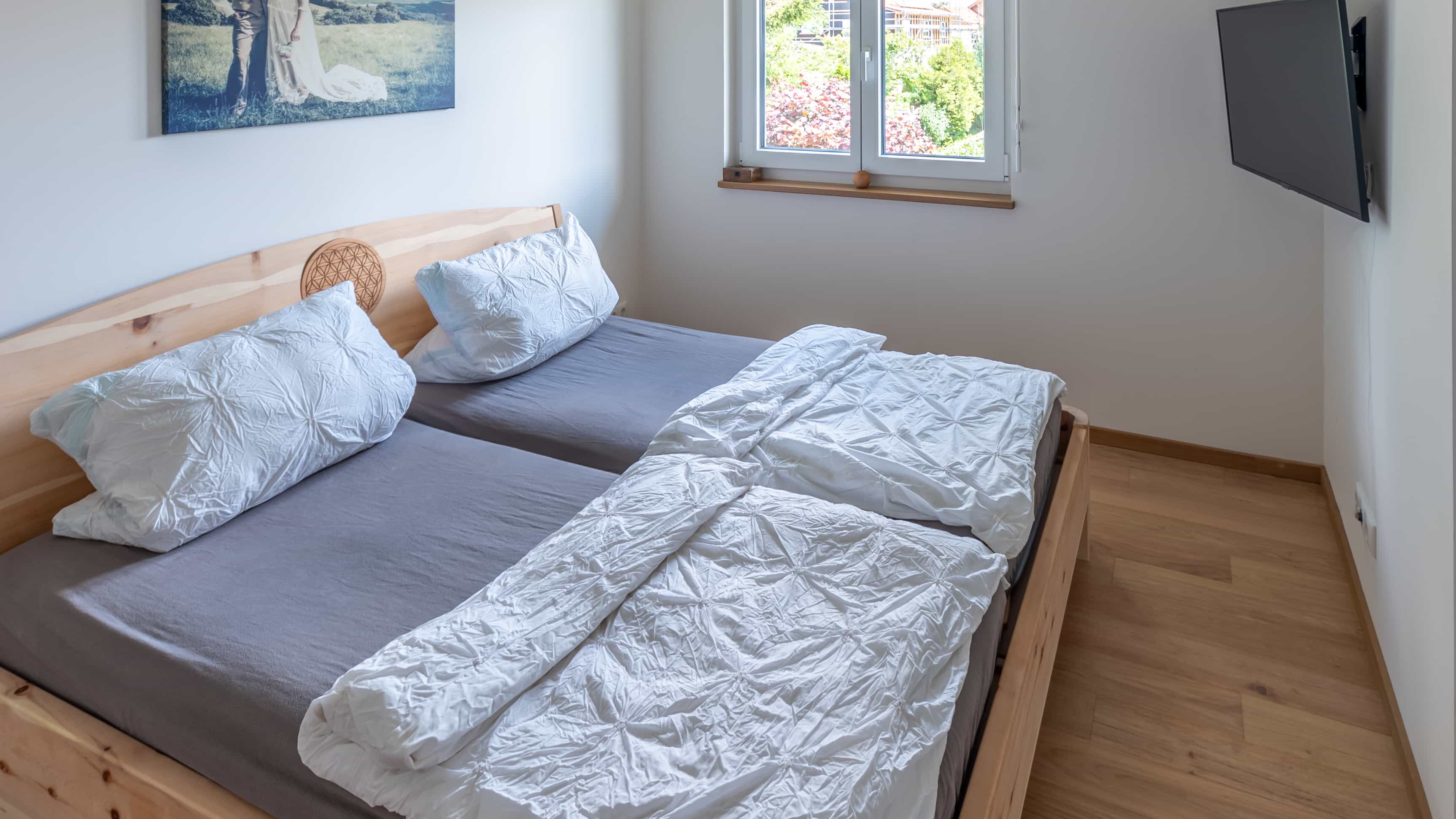 Doppelbett in hellem Schlafzimmer mit Holzfußboden, Fensterblick und Wandgemälde sowie moderner Hängeleuchte.