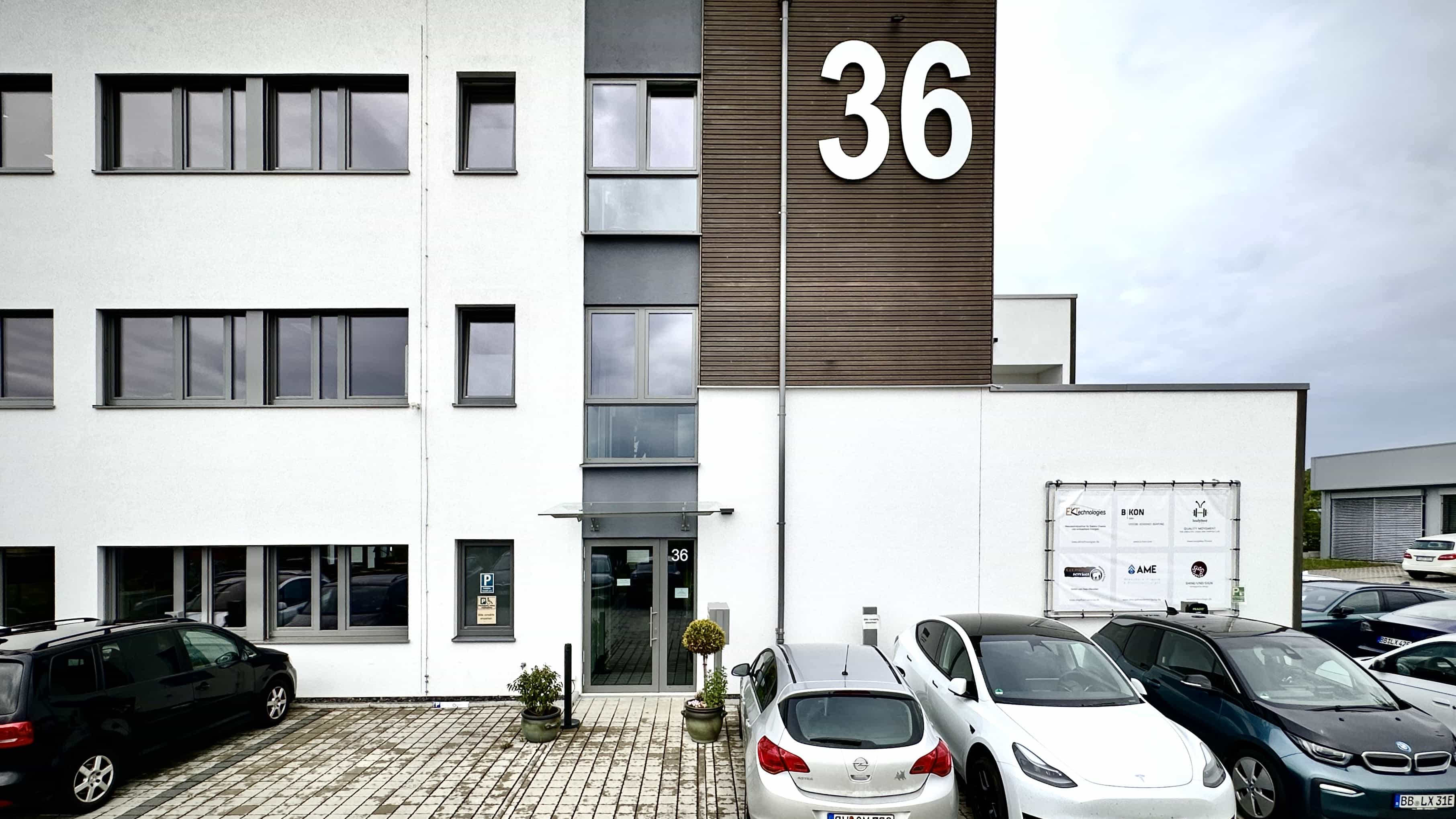 Eingangsfassade des Bürogebäudes LXinstruments mit Hausnummer 36 und parkenden Autos