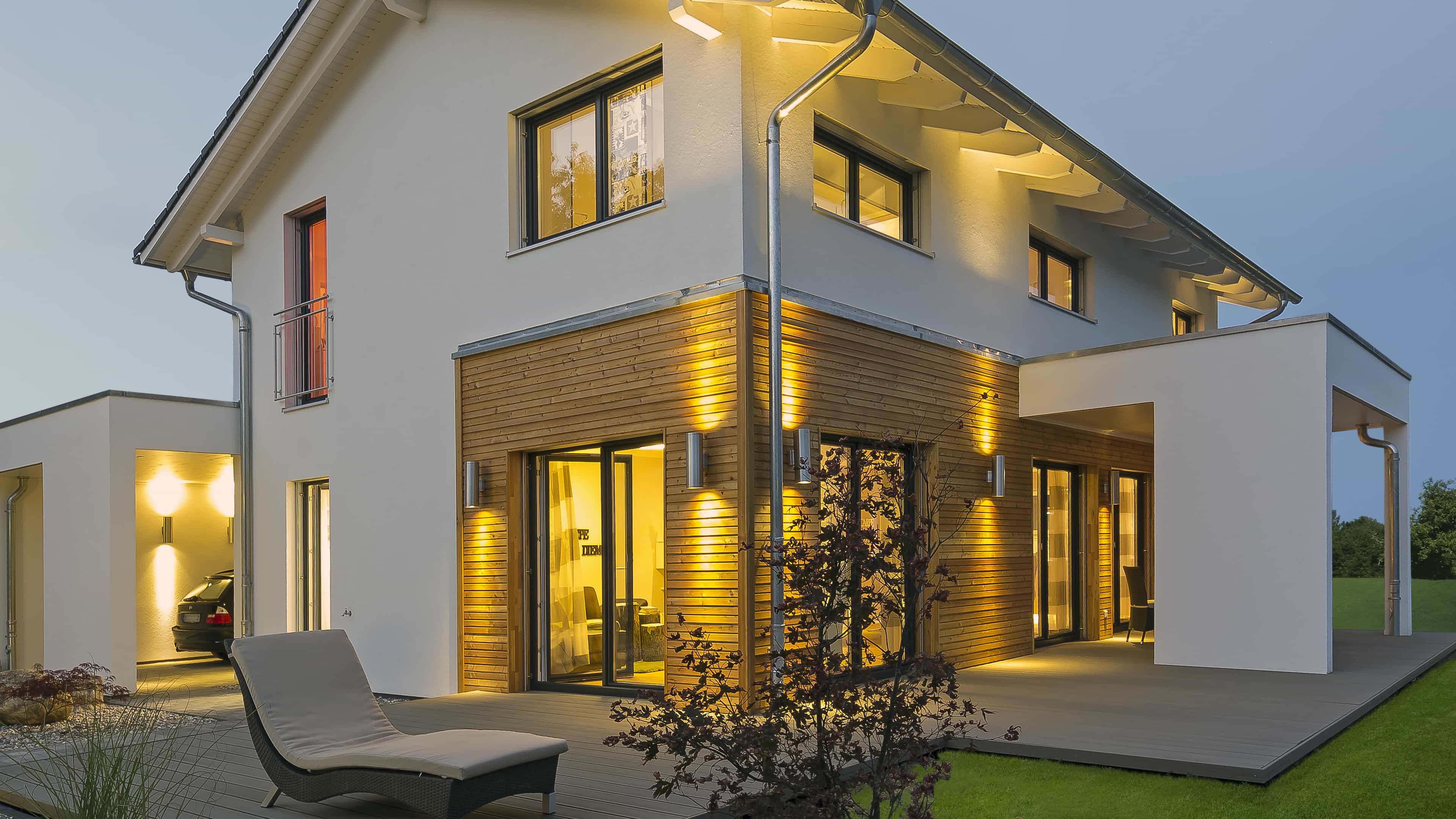 Musterhaus Haas MH Mannheim J 159 in der Dämmerung mit beleuchtetem Holzkubus und Carport