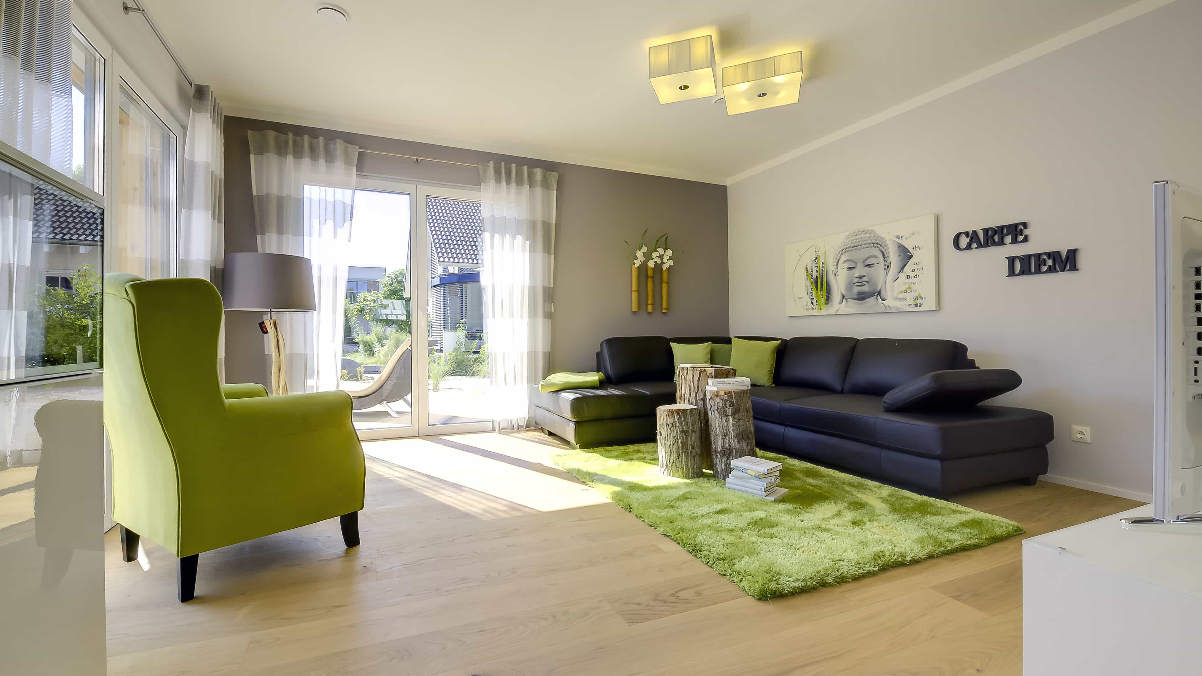 Wohnzimmer mit grünem Ohrensessel, schwarzem Sofa und grünem Teppich im Musterhaus Haas MH Mannheim J 159