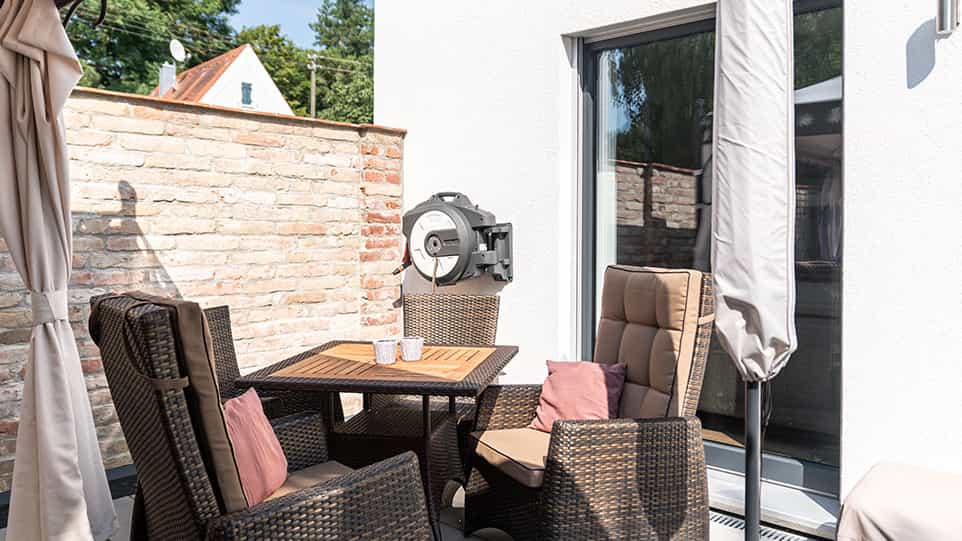 Terrasse mit Rattanmöbeln vor Ziegelmauer am Fertighaus der Familie Schmid